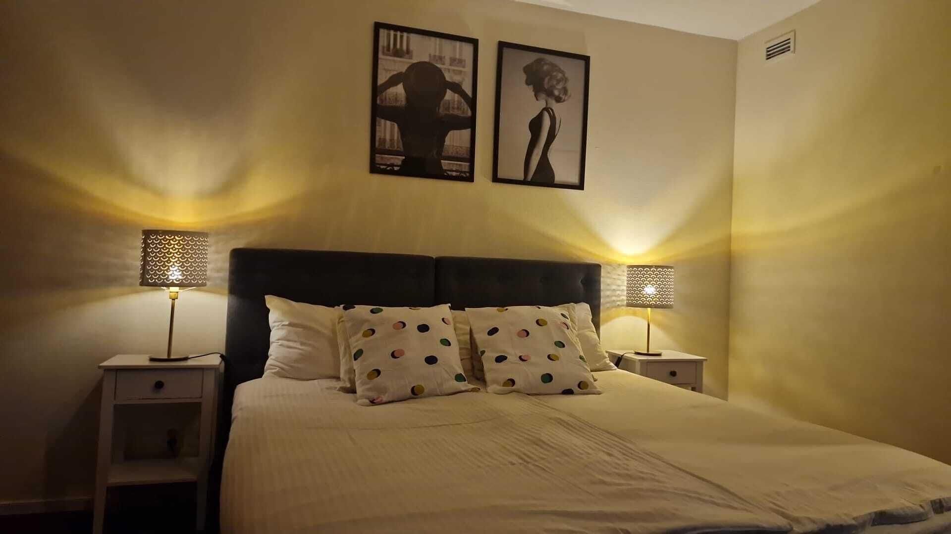 A neatly made bed with polka dot pillows, two bedside lamps, and two framed pictures on the wall.