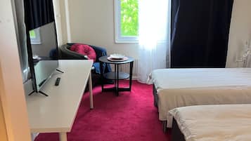 A hotel room with a desk, two beds, a small table, and a window with curtains.