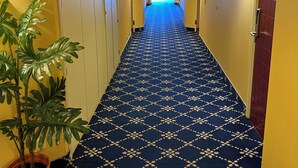 A hotel hallway with a patterned carpet, yellow walls, and a potted plant. - Noah Longstay  (Vasteras)