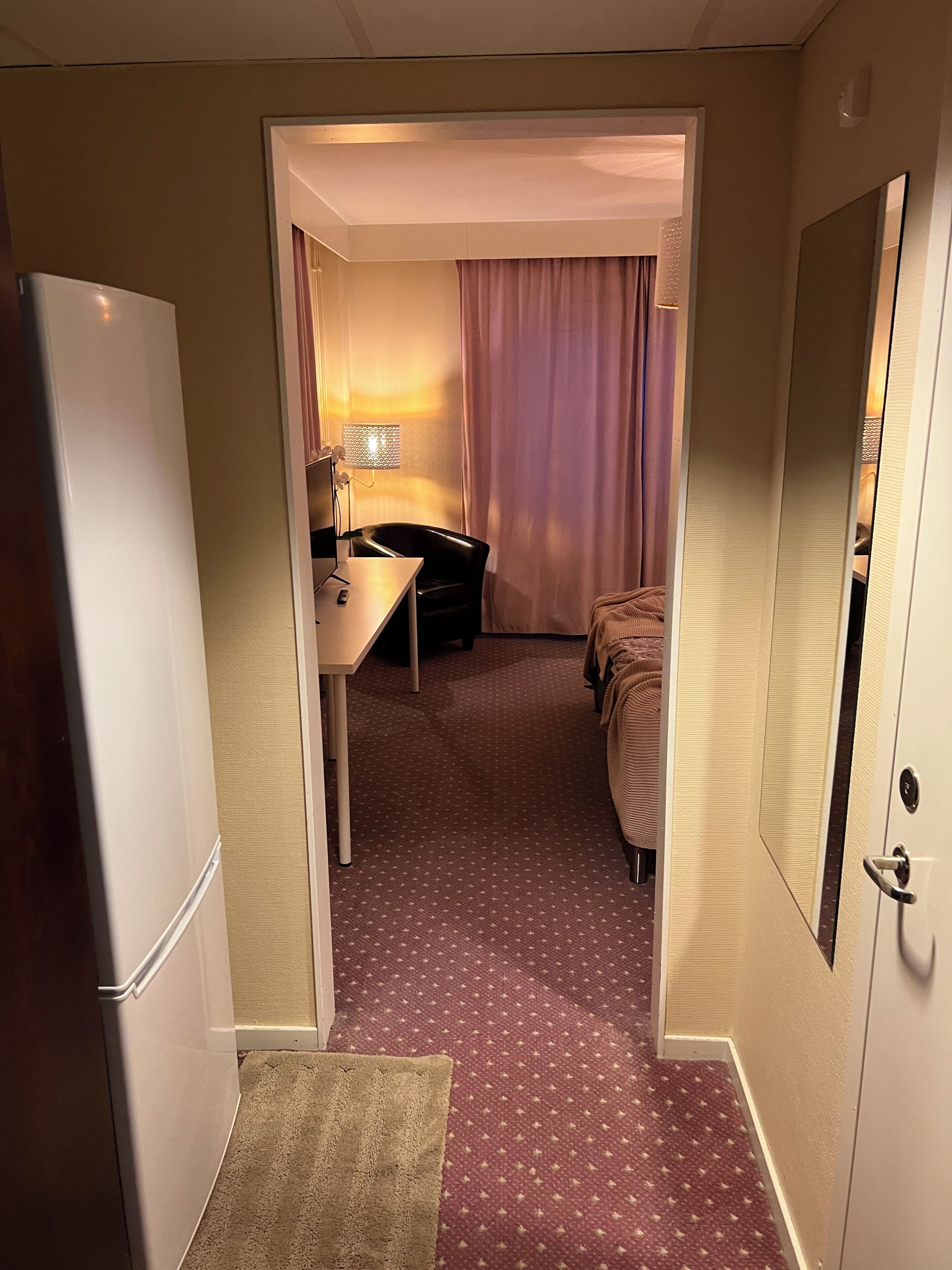 A hotel room with a bed, a desk, a lamp, and a mirror.
