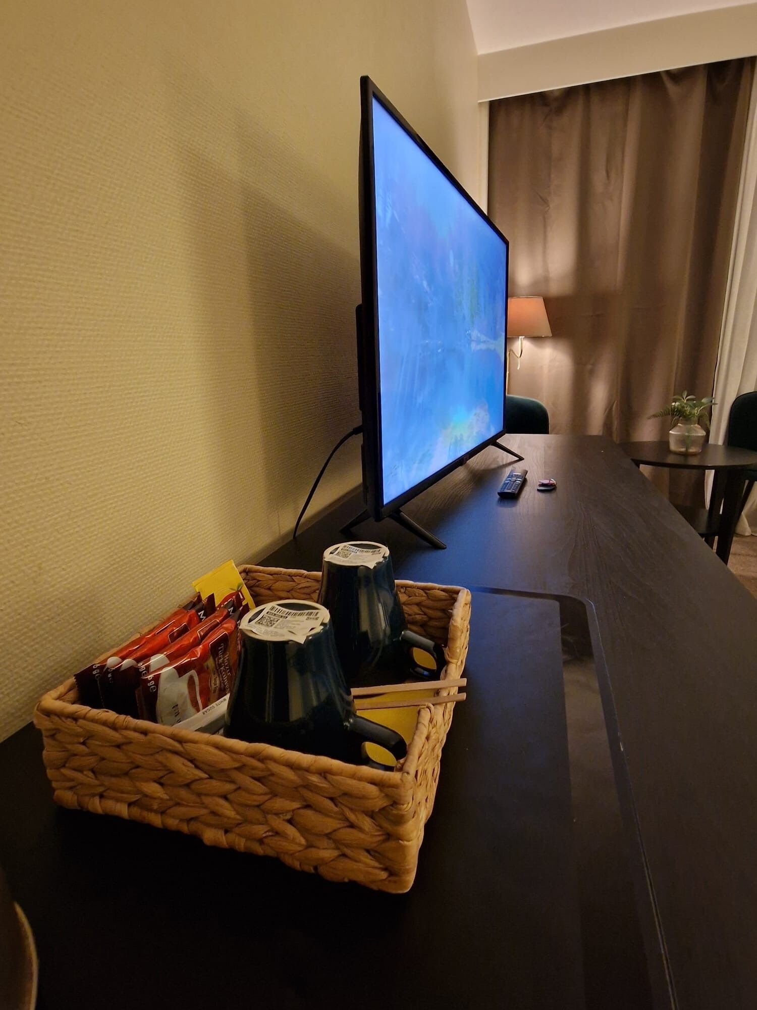 A television on a stand, a basket with bottles and packets, and a remote control on a table.