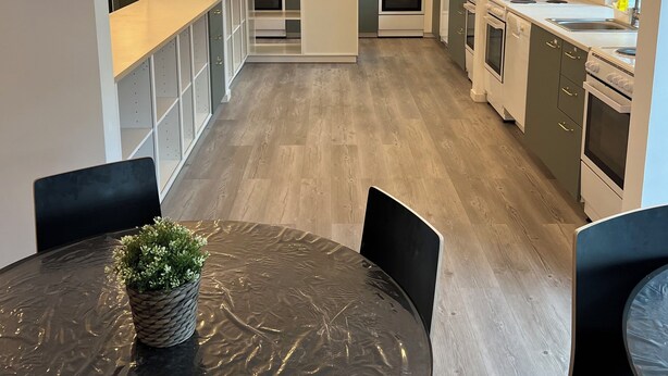 A modern kitchen with white cabinets, a central island, and a dining area with a round table and chairs. - Noah Longstay  (Vasteras)