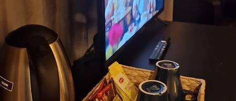 Un televisor sobre una mesa con aperitivos y una tetera.