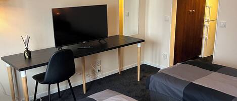 Habitación de hotel con cama, escritorio con computadora, silla, televisor y espejo.