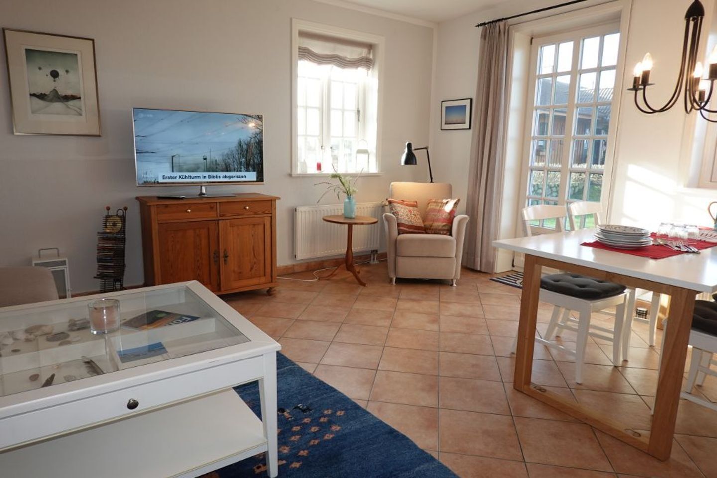 Una sala de estar con televisor, una mesita con un florero, una silla y un comedor con una mesa preparada para dos.