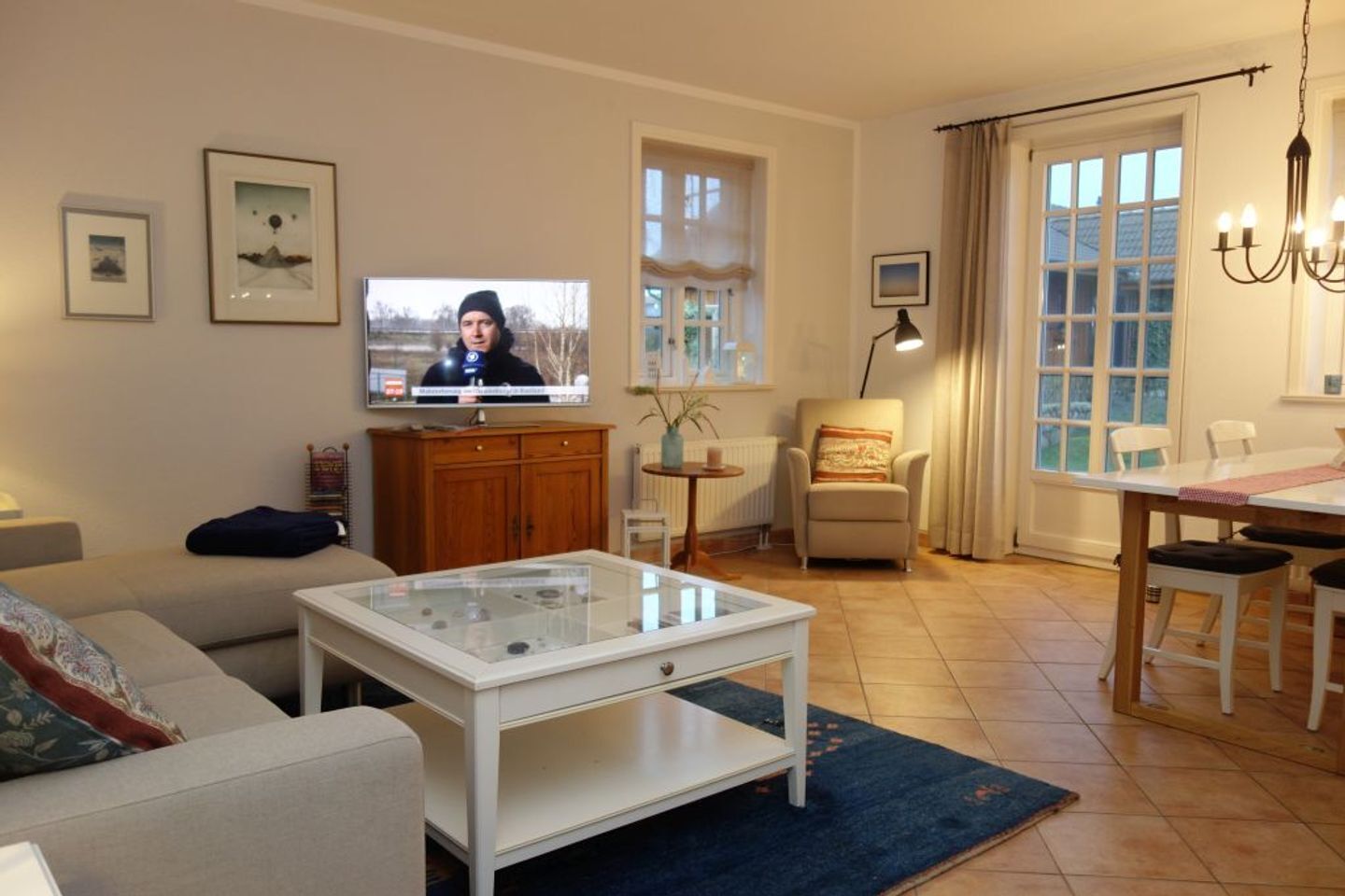 Sala de estar com sofá, mesa de centro, televisão, aparador de madeira, poltrona, mesa de jantar e lustre.