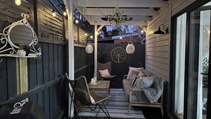 A cozy outdoor seating area with a cushioned bench, wicker chairs, and a dining table. - Warm Winter Escape | Fireplace and Charm (Bacchus Marsh)