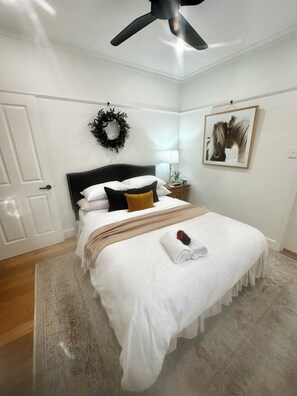 Cama bem arrumada com edredom branco, manta marrom e toalha enrolada com uma rosa vermelha.