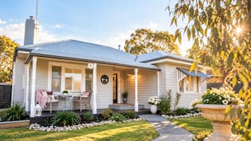 A house with a covered porch, a dining area with outdoor furniture, and a well-maintained garden.