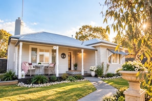 A house with a covered porch, a dining area with outdoor furniture, and a well-maintained garden. - Boutique Cottage in Bacchus Marsh.  Walking distance to town. (Bacchus Marsh)