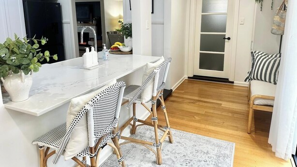 A modern kitchen with white cabinetry, a marble countertop, and a dining area with wicker chairs. - Warm Winter Escape | Fireplace and Charm (Bacchus Marsh)
