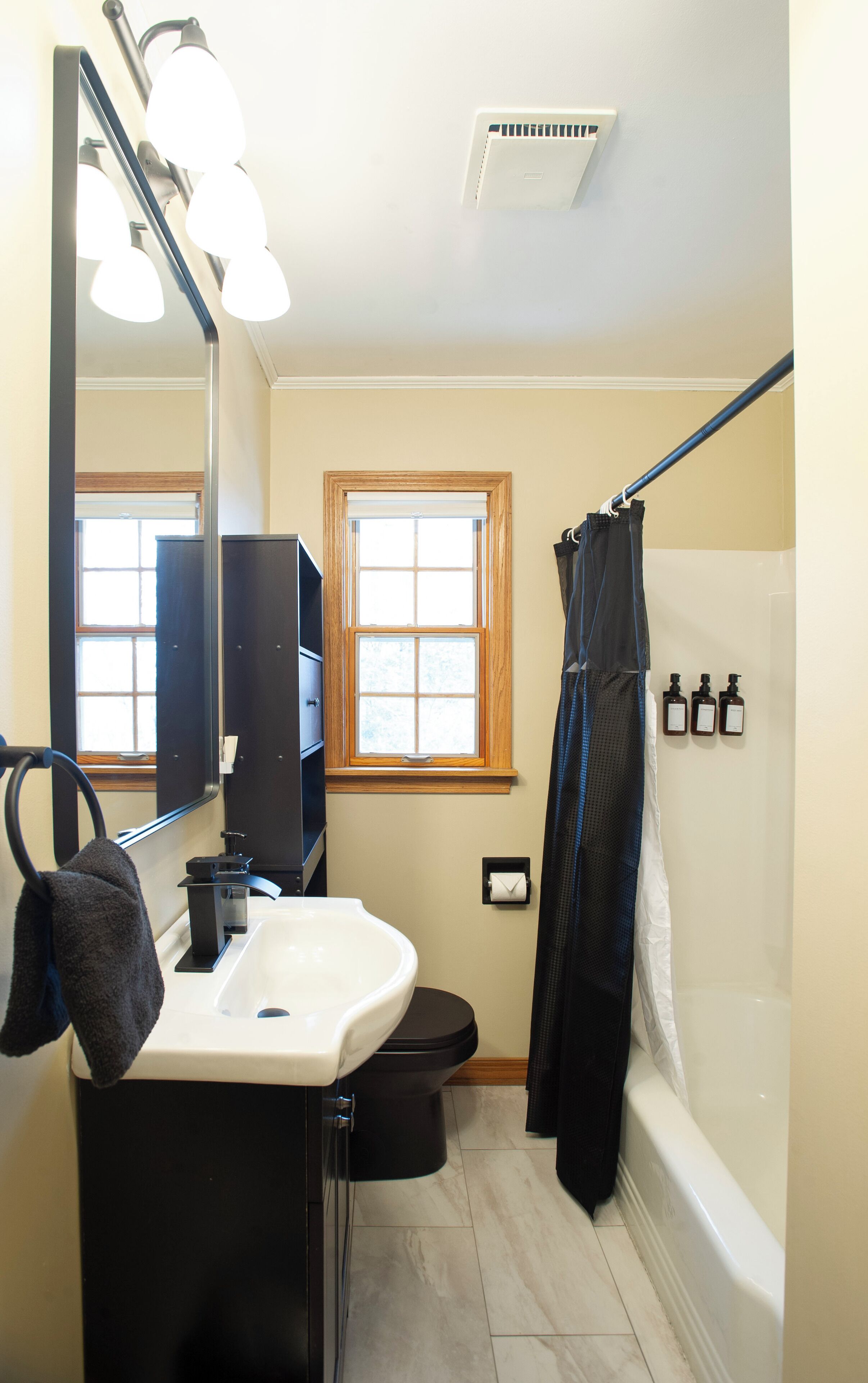 Un baño con lavamanos, espejo, ventana, ducha y tres botellas en la pared.