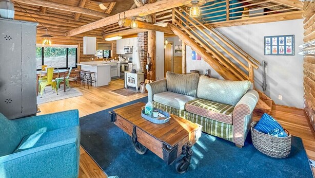 Un interior rústico con vigas de madera a la vista, una mesa de centro de madera, un sofá y una escalera.