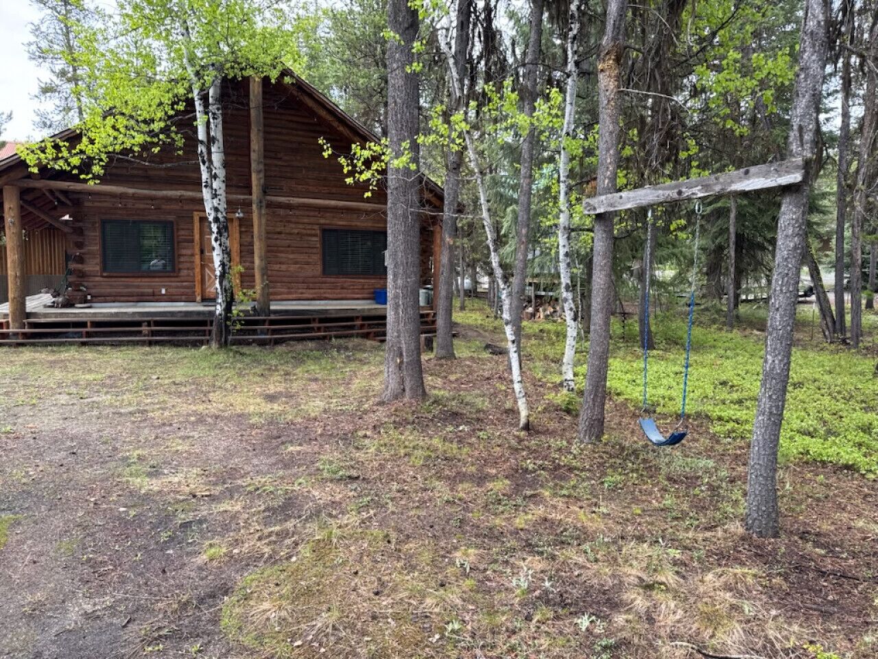 Een houten vakantiehuisje met een veranda en een schommel in een bebost gebied.