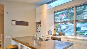 A modern kitchen with a large island, stainless steel appliances, and a view of a residential area through large windows. - Central Queenstown • 5BR 4.5BA Lake View Getaway (Queenstown)