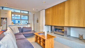 A modern living room with a sofa, a wooden coffee table, and a fireplace. - Central Queenstown • 5BR 4.5BA Lake View Getaway (Queenstown)