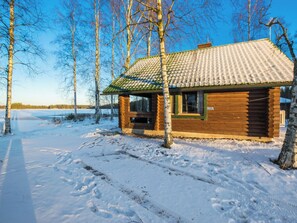 Puinen mökki, jonka katto on päällystetty tiilillä. Sen ympärillä on lumipeitteinen maa ja paljaita puita.
