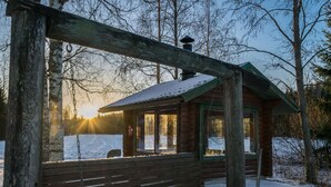 Eine Holzhütte mit einer Bank davor, umgeben von Schnee und Bäumen.