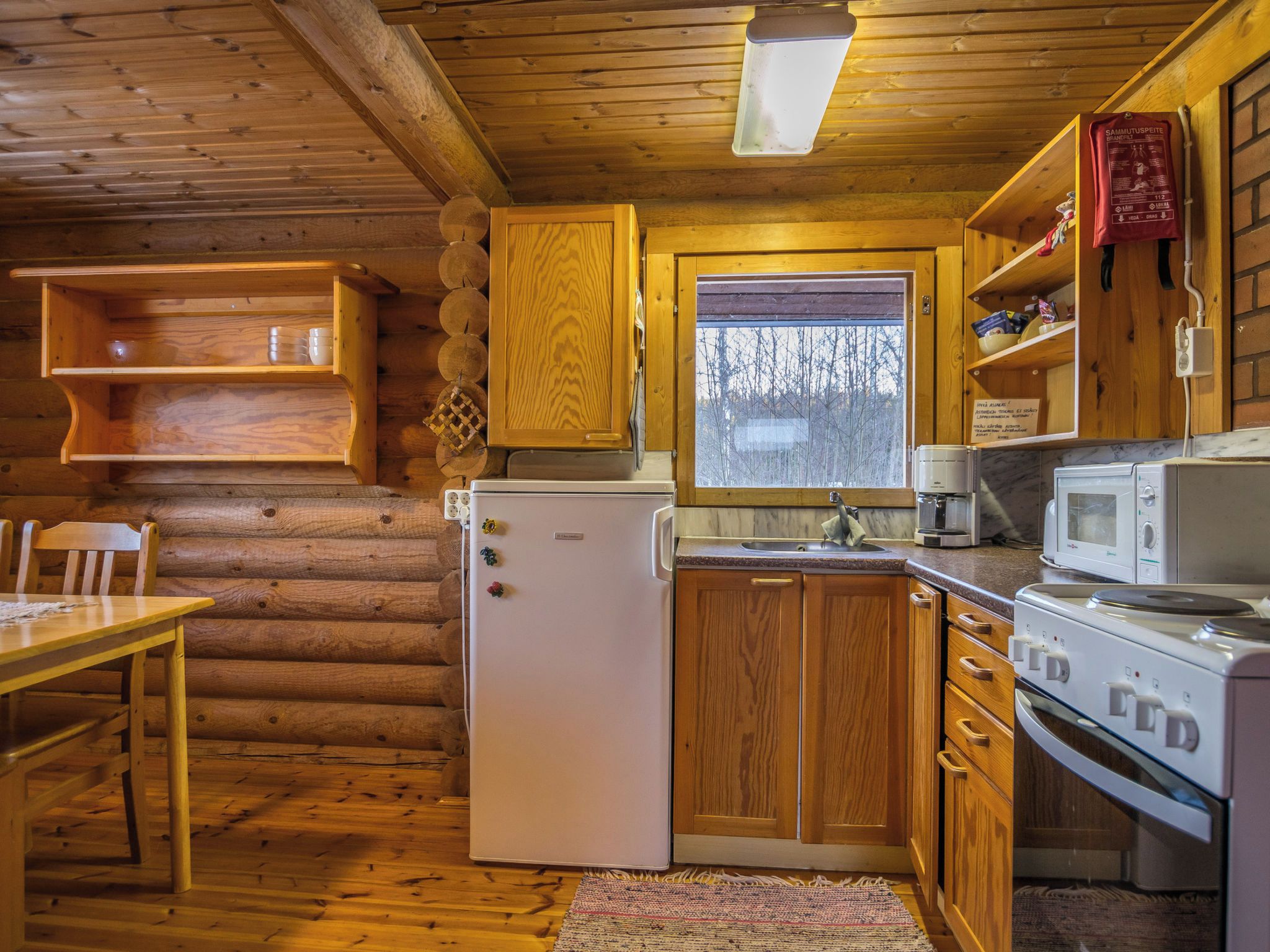 Una cucina compatta in una baita di legno, con mobili in legno, un frigorifero, un forno a microonde e un piano cottura.