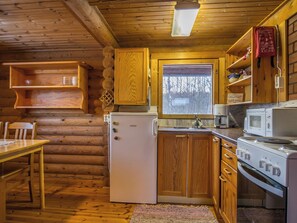 Kompakti hirsihirsimökkiin sijoitettu keittiö, jossa on puukaapit, jääkaappi, mikroaaltouuni ja liesi.