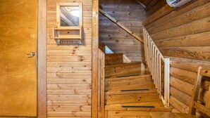 Ein Holzblockhaus-Interieur mit einer Holztreppe, einem kleinen Holzregal und einer Tür.