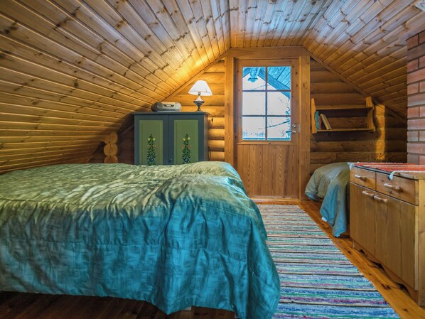 A cozy log cabin bedroom with a bed, a dresser, a lamp, and a window.