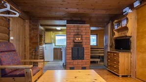 Ein Blockhaus-Interieur mit einem Holztisch, einer Couch, einem Kamin, einem Fernseher und einer Küchenzeile.