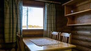 Ein Holzblockhaus-Interieur mit Esstisch, Stühlen, einem Fenster mit Vorhängen und einem Holzregal.