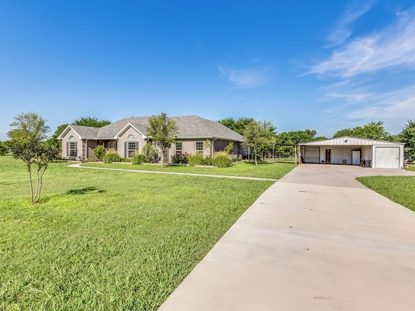 A single-story house with a garage, a well-maintained lawn, and a clear sky. - Charming 3 bedroom house in Pilot Point with WiFi, AC on 21 acres. (Pilot Point)