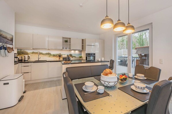 Cocina moderna con zona de comedor, que incluye una isla grande, luces colgantes y vistas a través del ventanal.
