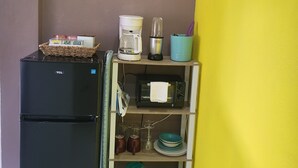 A kitchen with a black refrigerator, a coffee maker, a toaster, and a shelf with dishes and glasses. - The Local Experience - Kalbas Suite (Choiseul)