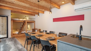 Un comedor moderno con una mesa de madera, sillas negras y una isla de cocina con fregadero.