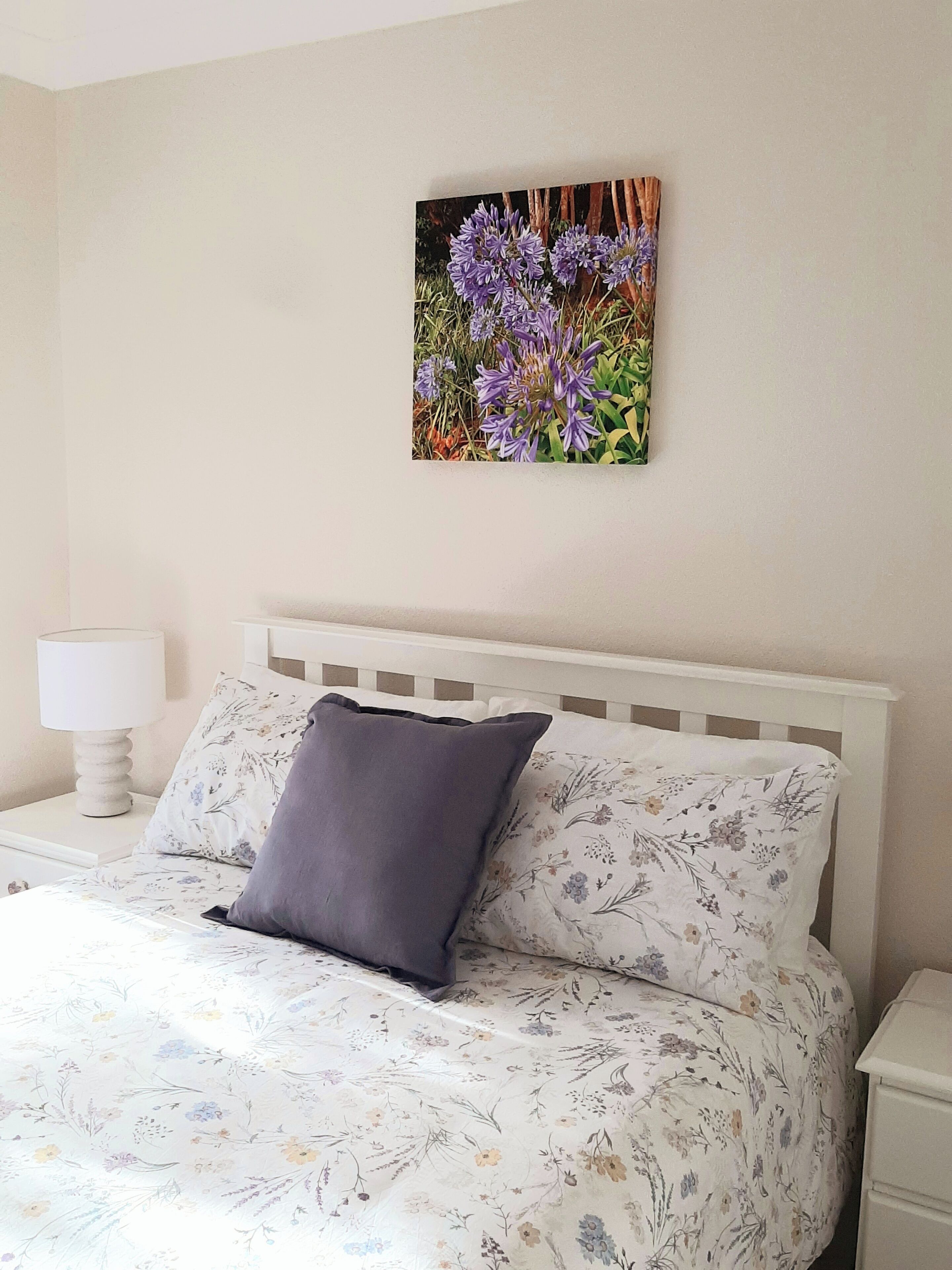 Quarto com cama, mesa de cabeceira, abajur e um painel de parede floral.