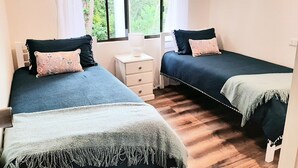A bedroom with two beds, a nightstand, and a window with curtains.