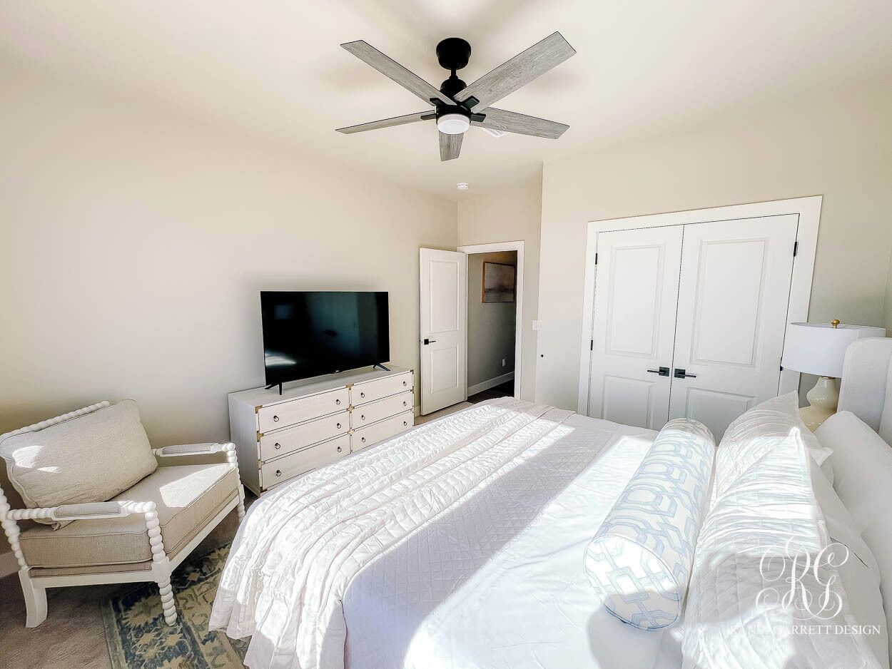 Ein Schlafzimmer mit Bett, Fernseher, Kommode, Stuhl und Deckenventilator.