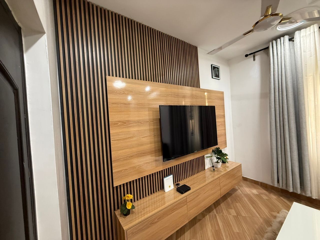 A modern living room with a flat-screen TV mounted on a wooden wall, a wooden console table, and a potted plant.