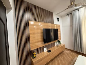 A modern living room with a flat-screen TV mounted on a wooden wall, a wooden console table, and a potted plant.