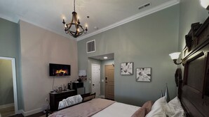 Une chambre à coucher avec un grand lit, un téléviseur fixé au mur, une commode et un lustre.
