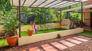 Un patio cubierto con pérgola, plantas en macetas, mobiliario exterior y un pequeño jardín.