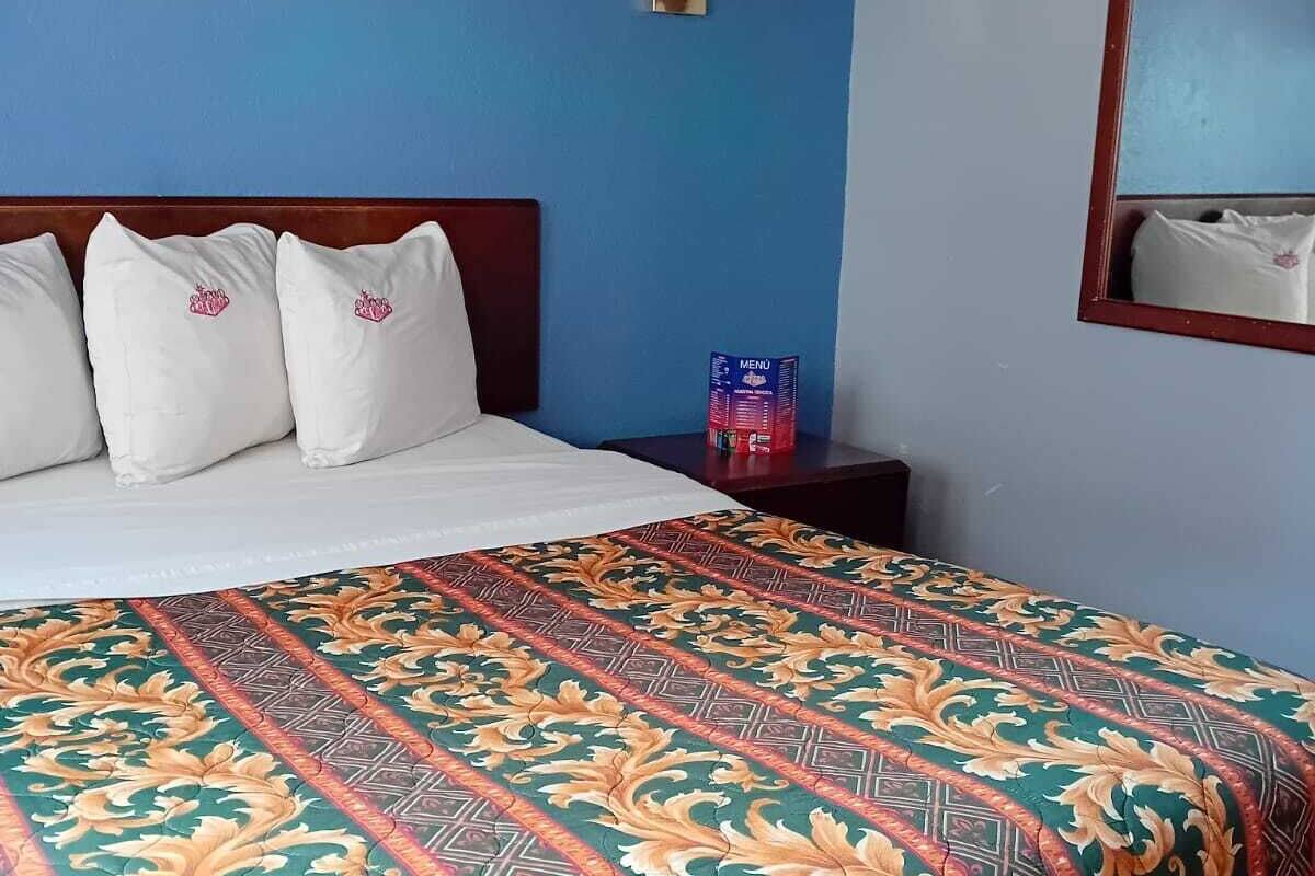 A hotel room with a bed, a nightstand, a wall-mounted lamp, and a mirror.