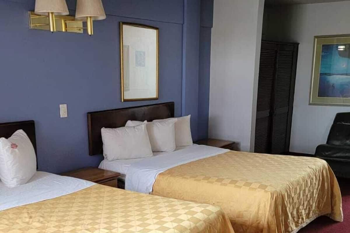 A hotel room with two beds, a framed picture on the wall, and a ceiling light.