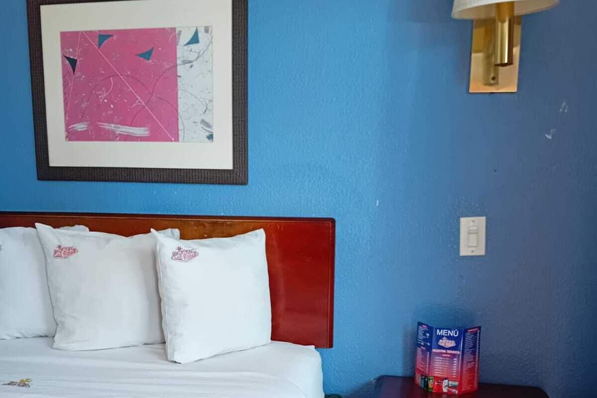 A hotel room with a bed, a nightstand, a framed picture, and a wall-mounted air conditioner.