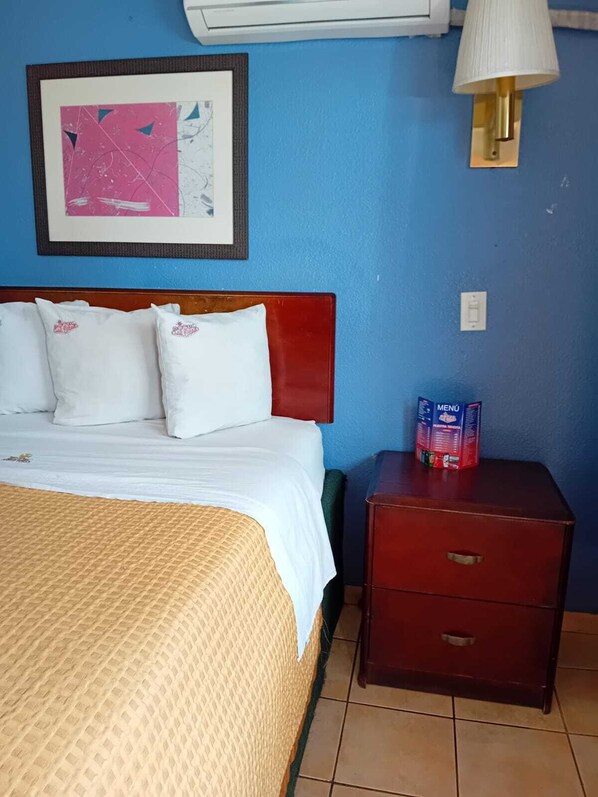 A hotel room with a bed, a nightstand, a framed picture, and a wall-mounted air conditioner. - HOTEL LAS VEGAS (Ensenada)