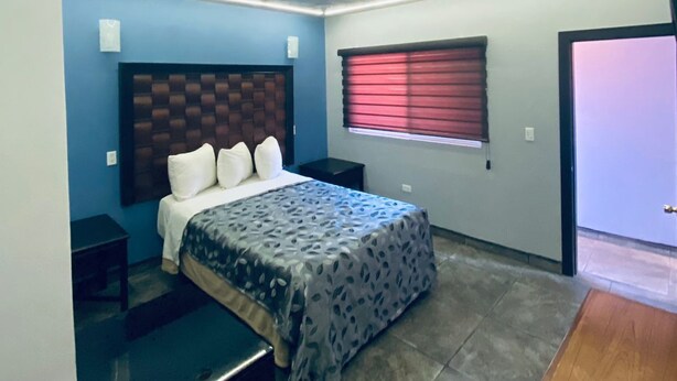 A modern bedroom with a bed, bedside tables, a window with blinds, and a door. - HOTEL LAS VEGAS (Ensenada)