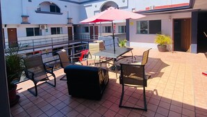 A covered outdoor patio with tiled flooring, outdoor seating, and a red umbrella. - HOTEL LAS VEGAS (Ensenada)