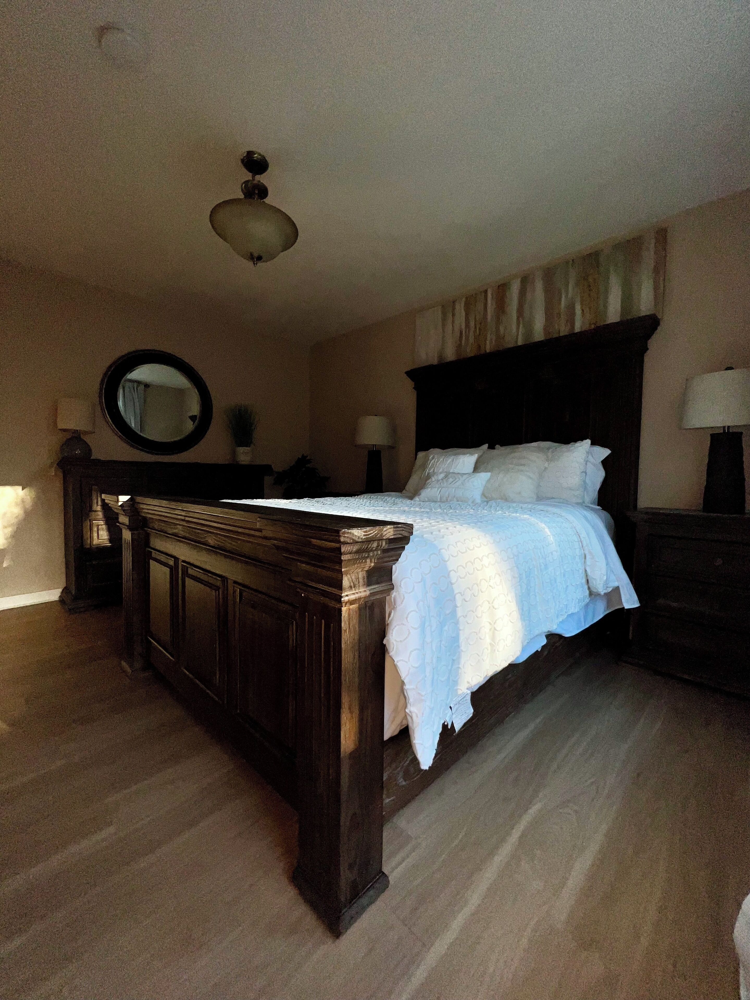 A bedroom with a wooden bed, a round mirror, and two bedside tables with lamps.
