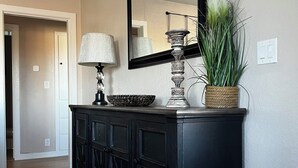 Een zwarte console tafel met een spiegel, een lamp en decoratieve voorwerpen in een gang.