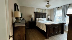 Een slaapkamer met een houten bed, twee nachtkastjes met lampen, een grote spiegel en een raam met gordijnen.