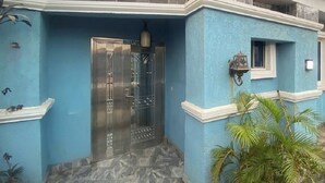 A house with a blue exterior, a tiled roof, a metal gate, and potted plants. - DE EMERITUS COURTYARD HOTEL (Abuja)