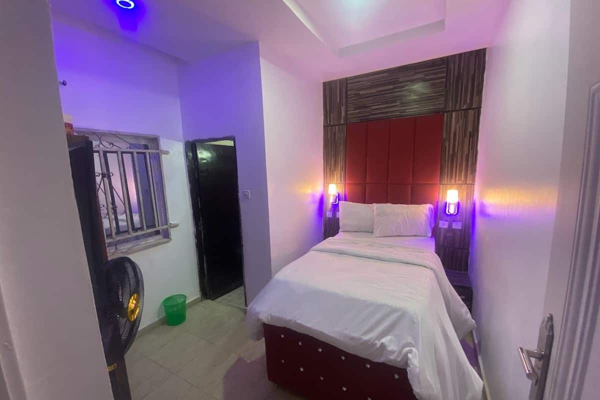 A bedroom with a bed, a fan, a door, and a window with a metal grill.